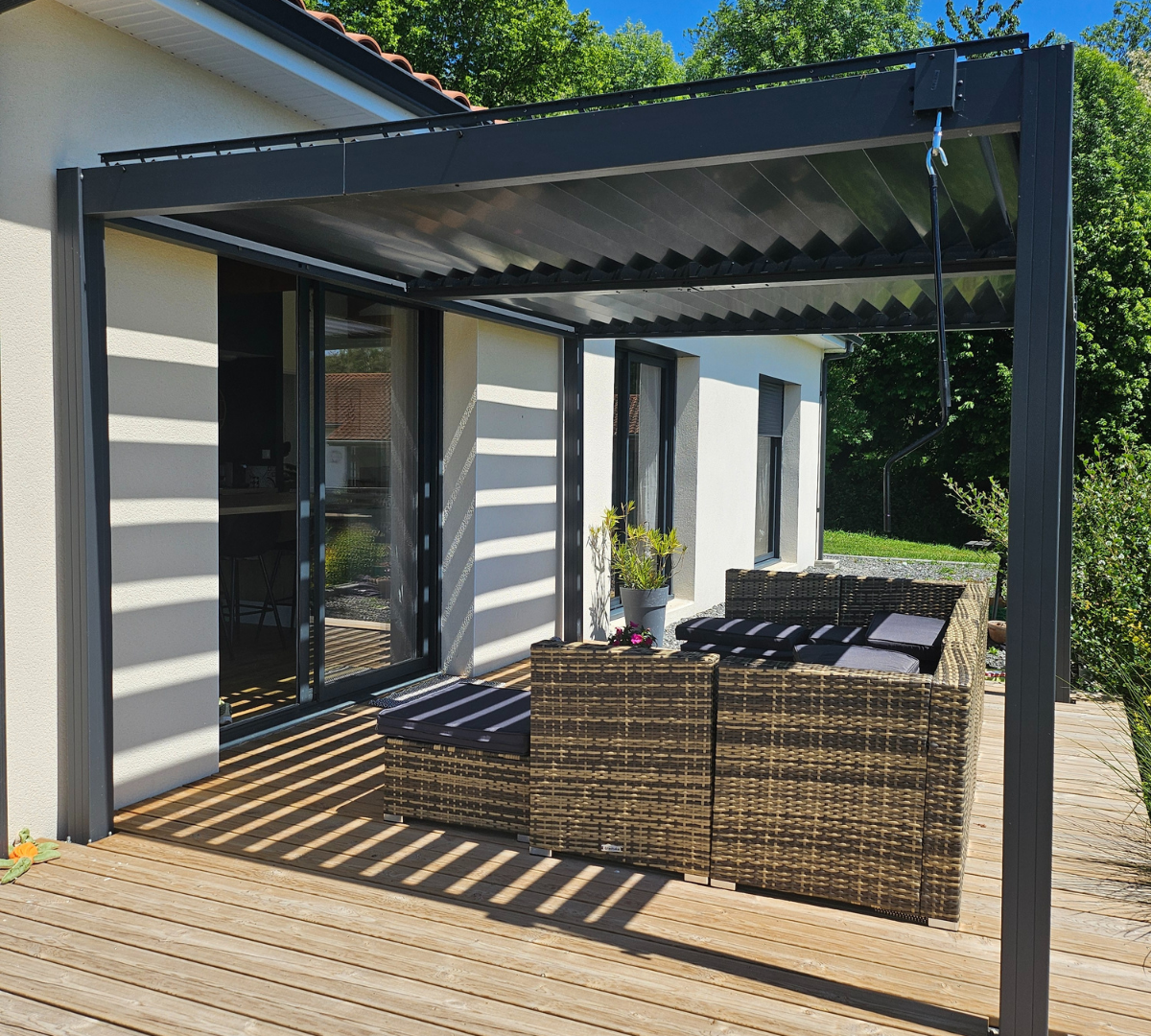 Profitez d’un espace extérieur moderne sublimé par une pergola bioclimatique en aluminium, véritable pièce maîtresse de cette terrasse. Sa structure élégante et contemporaine offre une protection optimale contre le soleil tout en laissant filtrer une lumière naturelle grâce à ses lames orientables. Cette pergola crée un jeu d’ombres raffiné sur le sol en bois, apportant fraîcheur et confort à tout moment de la journée. Idéale pour aménager un coin détente ou recevoir des invités, elle valorise l’esthétique de la maison tout en s’intégrant harmonieusement à l’environnement verdoyant. La pergola devient ici un atout incontournable pour profiter pleinement de la terrasse, quelle que soit la saison