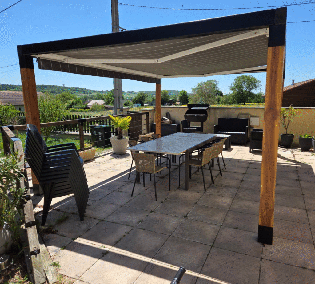 Pose d'une pergola avec des pieds en bois, et une structure supérieur en acier noir. La pergola est également équipé d'un store roulant.