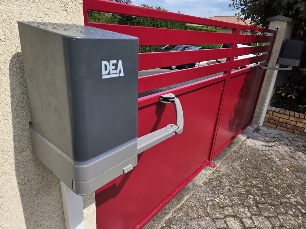 Zoom sur l'installation d'un moteur DEA, solution de motorisation haut de gamme pour portails battants. Ce modèle robuste et silencieux est idéal pour automatiser l'ouverture d’un portail en aluminium, comme celui présenté ici dans une teinte bordeaux éclatante. Fixé solidement au mur, le bloc moteur DEA est associé à un bras articulé discret qui garantit un mouvement fluide et sécurisé à chaque ouverture. Ce système allie fiabilité, design compact et performance, même en usage intensif. Un choix parfait pour ceux qui souhaitent conjuguer confort d’utilisation, sécurité et esthétique moderne.