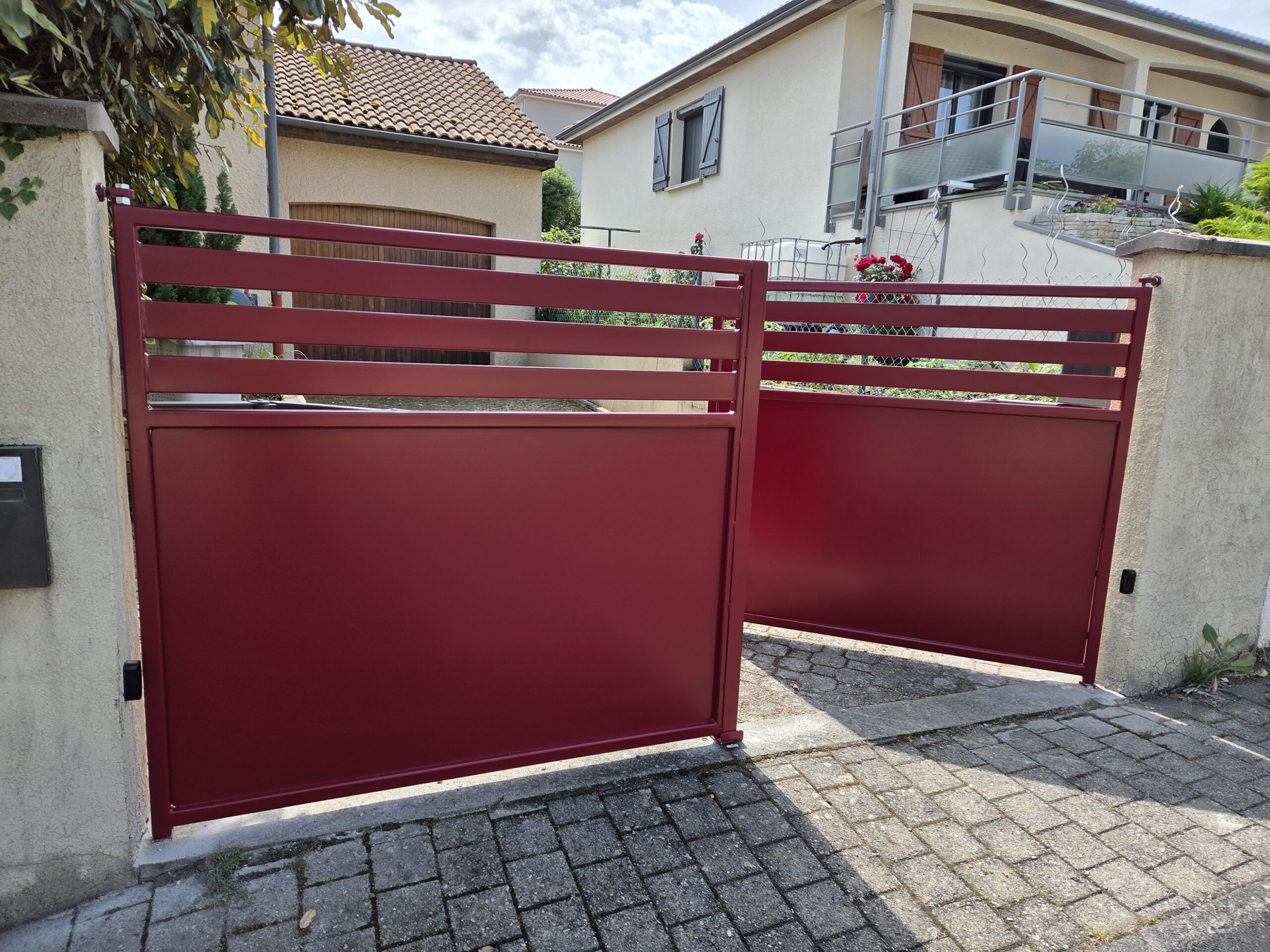 Découvrez notre dernier projet de portail moderne en aluminium thermolaqué, ici présenté dans une élégante finition bordeaux. Alliant design épuré et robustesse, ce portail à lames horizontales ajourées offre un parfait équilibre entre intimité et esthétisme. Conçu pour s’intégrer harmonieusement dans un environnement résidentiel, il assure à la fois sécurité et style grâce à sa structure solide et son système d’ouverture motorisée discrètement intégré. Le rendu satiné du laquage reflète subtilement la lumière naturelle, ajoutant une touche de modernité à l’entrée de votre propriété. Un choix idéal pour ceux qui recherchent une solution à la fois durable, esthétique et contemporaine.