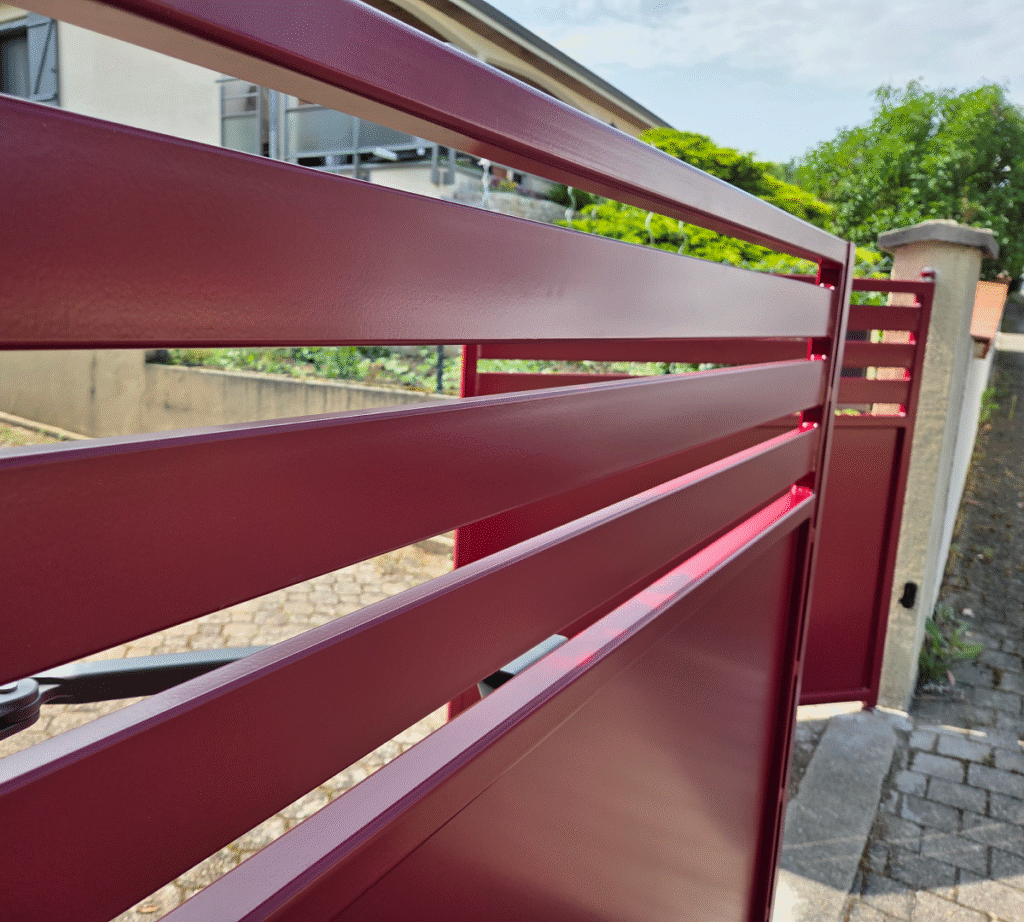 Découvrez notre dernier projet de portail moderne en aluminium thermolaqué, ici présenté dans une élégante finition bordeaux. Alliant design épuré et robustesse, ce portail à lames horizontales ajourées offre un parfait équilibre entre intimité et esthétisme. Conçu pour s’intégrer harmonieusement dans un environnement résidentiel, il assure à la fois sécurité et style grâce à sa structure solide et son système d’ouverture motorisée discrètement intégré. Le rendu satiné du laquage reflète subtilement la lumière naturelle, ajoutant une touche de modernité à l’entrée de votre propriété. Un choix idéal pour ceux qui recherchent une solution à la fois durable, esthétique et contemporaine.