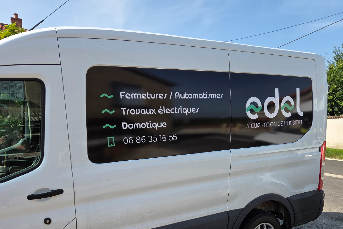 EDEL Électricien : Photo du camion EDEL. On voit le côté du camion, avec le logo EDEL, avec les services de Fermetures / Automatismes, Travaux électriques et Domotique.